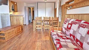 Un salon chaleureux avec des meubles en bois, un canapé recouvert d’un tissu à motifs et un coin repas comprenant des chaises et une table.