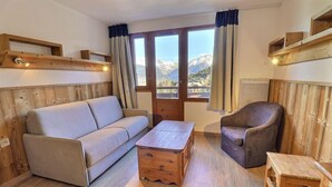 Una habitación acogedora con sofá, sillón, mesa de centro de madera y vistas a las montañas a través de amplias ventanas.