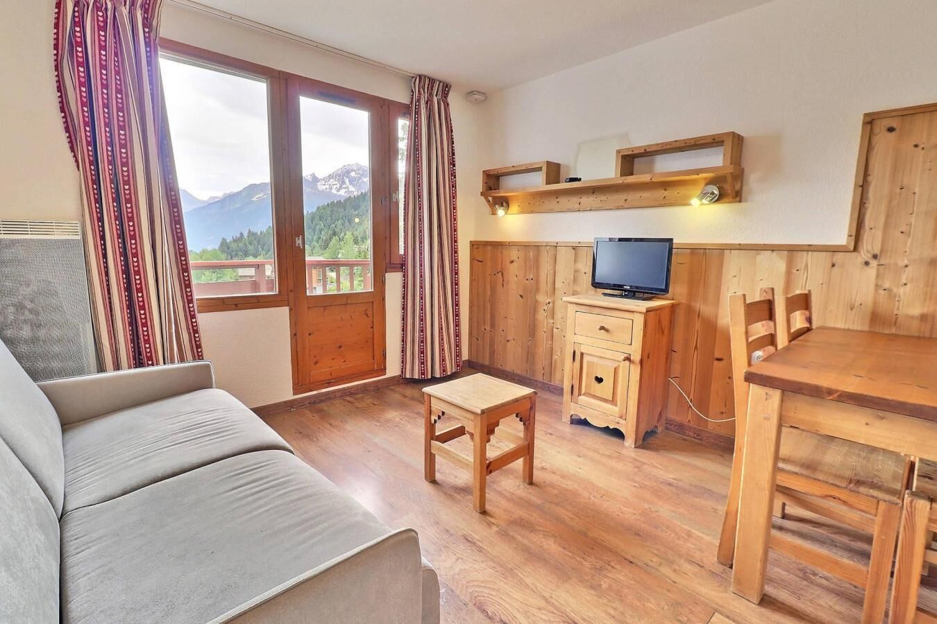 Una habitación acogedora con un sofá, una pequeña mesa de madera, un televisor sobre un mueble de madera y una mesa de comedor con sillas.