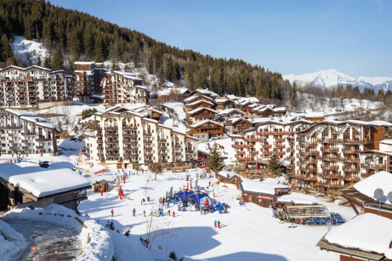 Une station de ski comprenant plusieurs bâtiments de style chalet, des toits enneigés et un paysage montagneux en toile de fond.