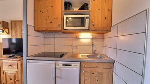 Una cocina compacta con armarios de madera, un microondas, un lavamanos y un lavavajillas.