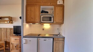 Une cuisine compacte avec des meubles en bois, un four à micro-ondes, un évier, un lave-vaisselle et un téléviseur posé sur un meuble en bois.