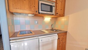 A compact kitchen with wooden cabinets, a microwave, a sink, and a dishwasher.