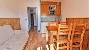 A compact living space with a kitchenette, a dining area with wooden furniture, and a sofa.