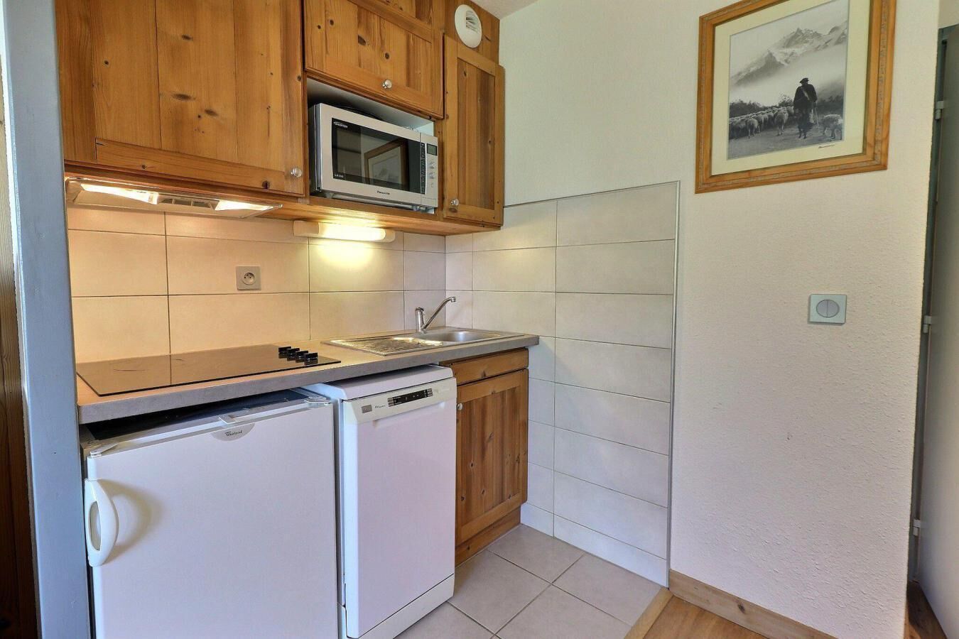 A compact kitchen with wooden cabinets, a microwave, a dishwasher, and a sink.