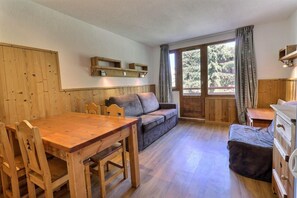 A cozy room with a wooden dining table, a sofa, and a small cabinet. - 150m from resort center, 9th floor, balcony, ski locker, 31m², La Tania (Courchevel)