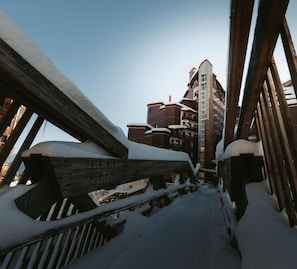 Un escalier en bois recouvert de neige mène à un immeuble à plusieurs étages doté de balcons.