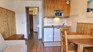 Une cuisine compacte dotée de meubles en bois, d’un four à micro-ondes et d’un lave-vaisselle. Un coin repas est aménagé avec une table et des chaises en bois.