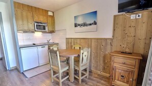 Une cuisine compacte avec des meubles de rangement en bois, un four à micro-ondes, une table à manger avec des chaises et un petit meuble en bois.