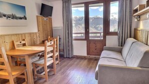 Un salon chaleureux avec une table à manger en bois, des chaises, un canapé et un téléviseur fixé sur un meuble en bois.