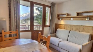 Une pièce chaleureuse avec une table et des chaises en bois, un canapé et une fenêtre donnant sur les montagnes.