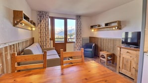 A cozy room with a wooden bed, a small desk, a chair, and a TV. - 150m from resort center, 9th floor, balcony, ski locker, 31m², La Tania (Courchevel)
