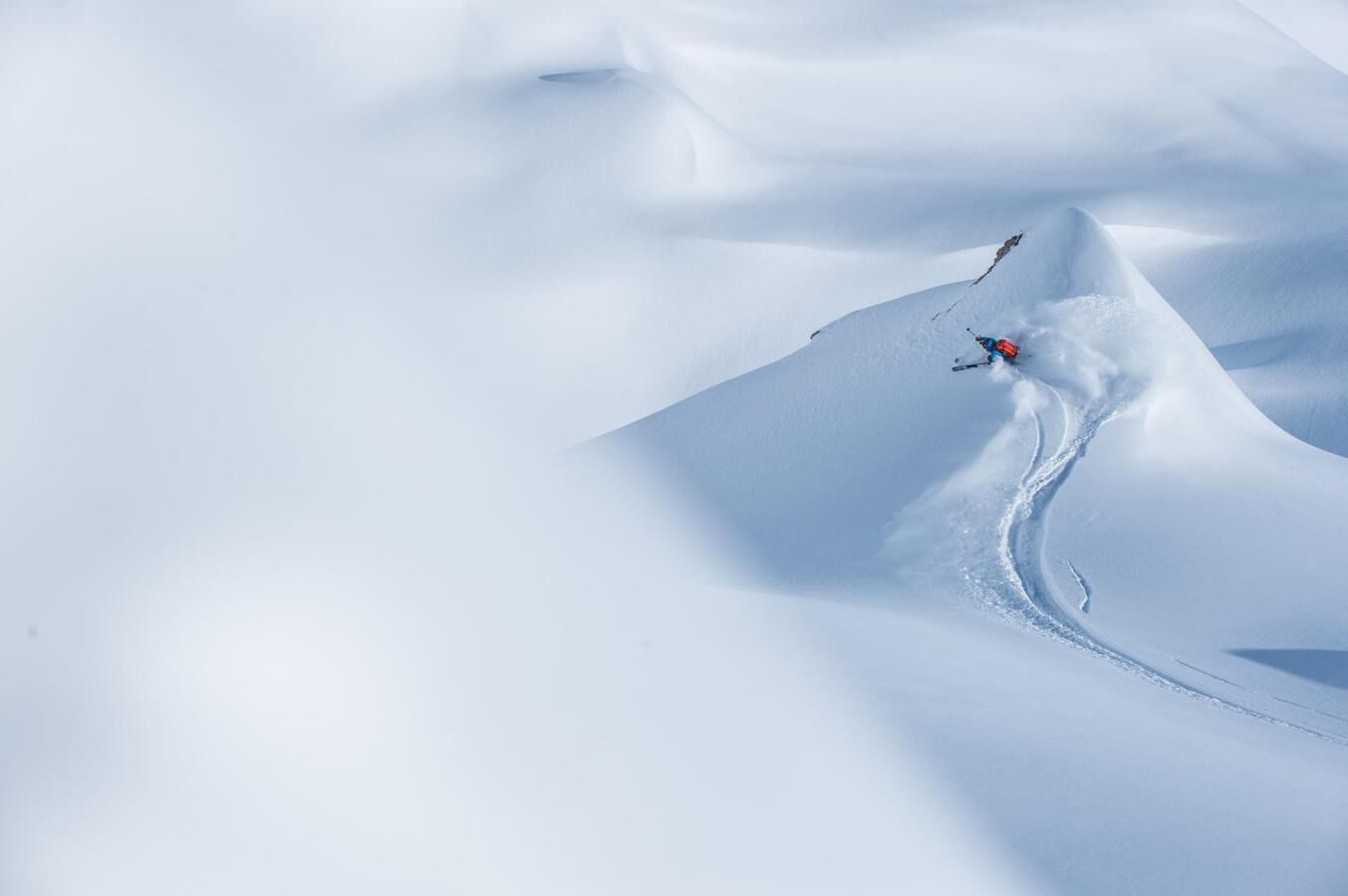 A snowy mountain landscape with a skier carving a path through the snow.