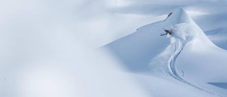 A snowy mountain landscape with a skier carving a path through the snow.