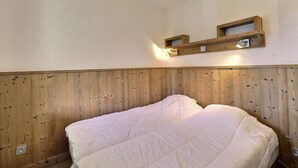 A room with a wooden headboard, a bed with white bedding, and two wall-mounted shelves above the bed.