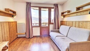 A cozy room with a wooden floor, a sofa, a radiator, and a window with curtains.