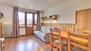 A cozy room with a wooden floor, a sofa, a dining table with chairs, and a window with curtains.