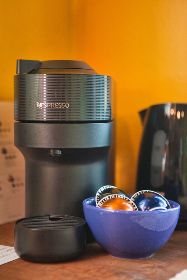 Una máquina de café Nespresso, un tazón azul con cápsulas de café y un recipiente negro sobre una superficie de madera.
