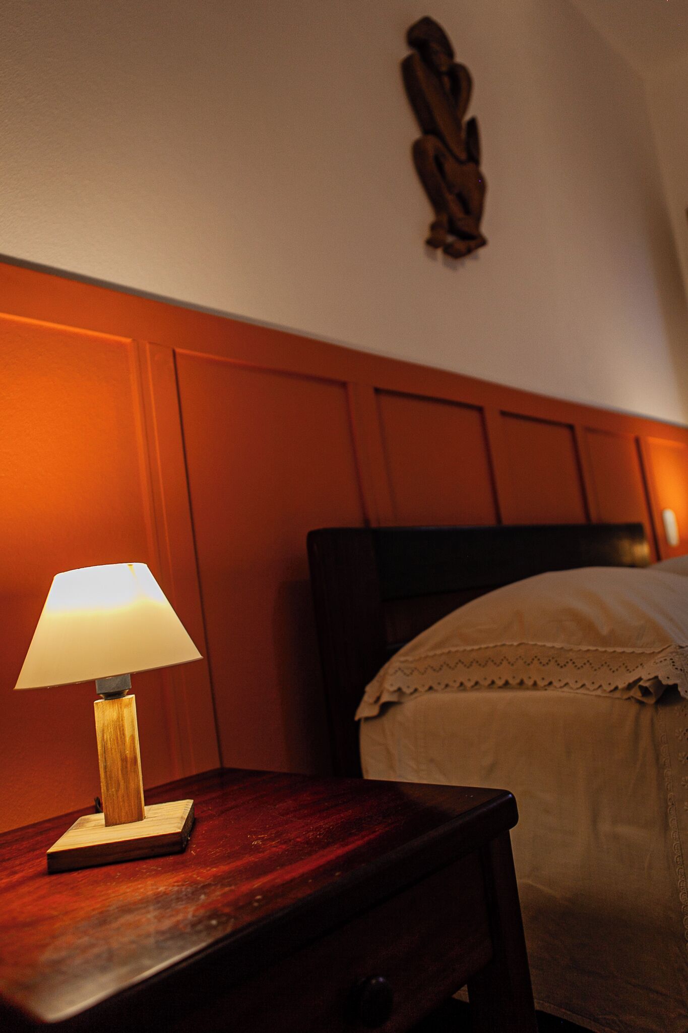 A wooden nightstand with a lamp, a bed with white bedding, and a wooden headboard.