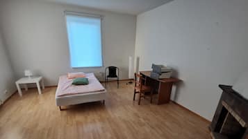 A bedroom with a bed, a desk, a chair, a small table, and a window.