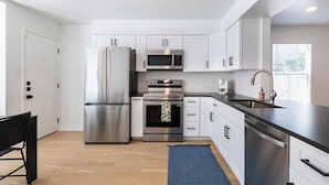 A modern kitchen with stainless steel appliances, white cabinetry, and a black countertop. - Spacious 2 Bedroom East Riverside Home with Garage and Yard (Austin)