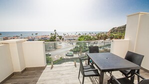A balcony with a table and chairs, overlooking a coastal town with palm trees and a road. - Paloma Beach apartment 3.2a (Manilva)