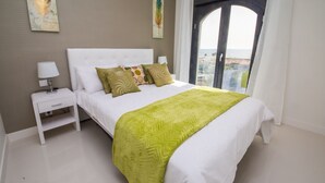 A neatly arranged bedroom with a bed, a bedside table with a lamp, and a view of the sea through a large window. - Paloma Beach apartment 3.2a (Manilva)