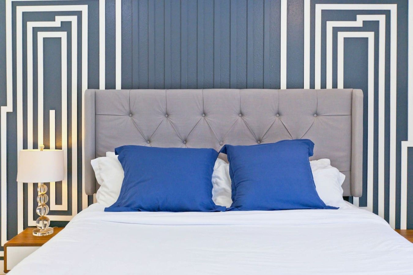 A bed with a tufted headboard, white bedding, and two blue pillows.
