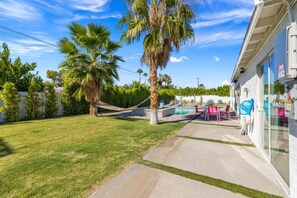 A backyard with a swimming pool, palm trees, and a patio with chairs.