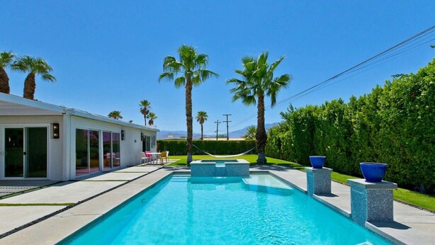 A modern pool with clear blue water, surrounded by palm trees and a white building with large windows. - Azul Desert Escape with Pool & Views (Palm Springs)