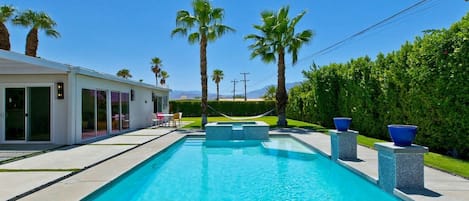 A modern pool with clear blue water, surrounded by palm trees and a white building with large windows.