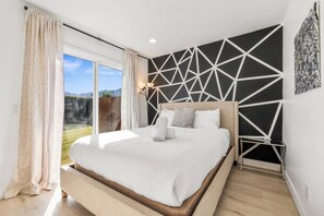 A bedroom with a large bed, a view of the outdoors, and a geometric wall design.