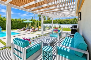 Un espacio al aire libre techado con piscina, sillones de descanso y una parrilla.