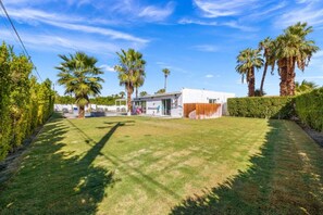 A residential property with a well-maintained lawn, palm trees, and a modern house with a white exterior.