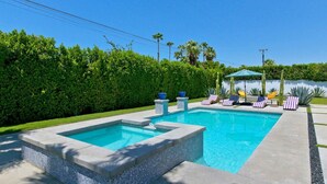 A rectangular swimming pool with a tiled edge, surrounded by a hedge, and a gazebo with chairs in the background. - Azul Desert Escape with Pool & Views (Palm Springs)