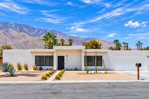 Una casa moderna de dos pisos con garaje, rodeada de vegetación desértica y montañas.