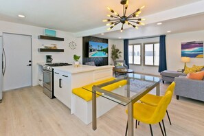 A modern kitchen with a central island, a dining area with yellow chairs, and a living room with a sofa and a painting.