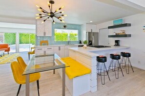Una cocina moderna con una isla central, taburetes de bar y una zona de comedor con sillas amarillas.