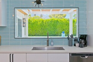 A kitchen with a large window, a sink, a coffee maker, and cabinets.
