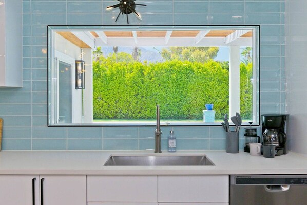A kitchen with a large window, a sink, a coffee maker, and cabinets.