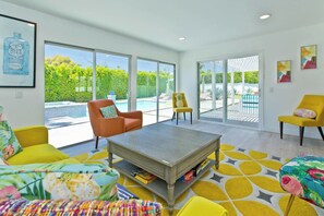 A spacious living room with a large window, a coffee table, and vibrant yellow and orange furniture.