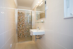 Un baño moderno con cabina de ducha de vidrio, un lavabo blanco y un espejo sobre él.