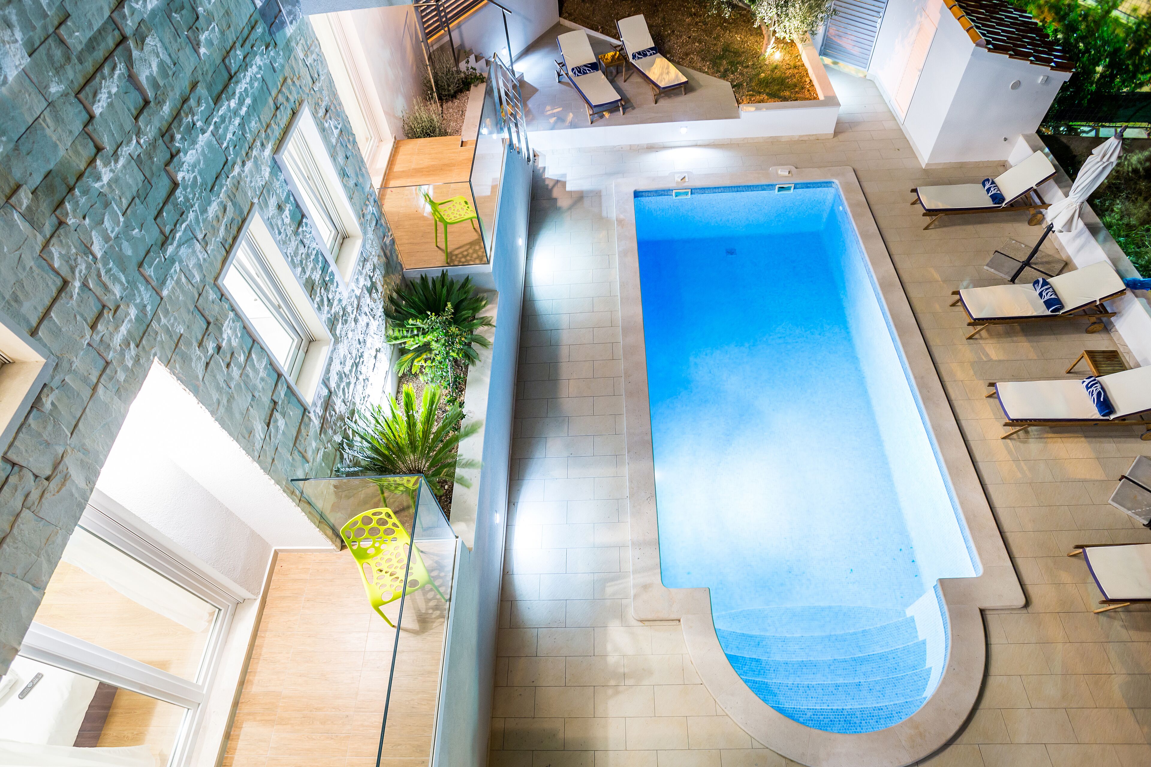 An indoor swimming pool with a tiled deck, lounge chairs, and potted plants.
