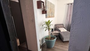 Een woonkamer met een houten vloer, een blauwe plant in een pot, een grijze bank en een schilderij aan de muur.