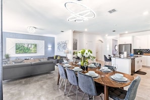 Une cuisine moderne avec des meubles blancs, un réfrigérateur en acier inoxydable et un coin repas comprenant une table en bois et des chaises grises.