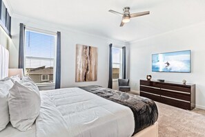 Ein Schlafzimmer mit einem Bett, einem Deckenventilator, einem Fernseher und einem Fenster mit Jalousien.