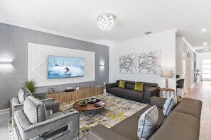Ein modernes Wohnzimmer mit Flachbildfernseher, grauen Sofas, einem Couchtisch und abstrakter Wandkunst.