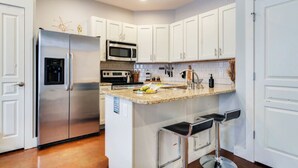 A modern kitchen with white cabinets, stainless steel appliances, a granite countertop, and two bar stools.