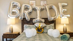 A bed with a patterned bedspread, a decorative headboard, and a 'BRIDE' balloon decoration.