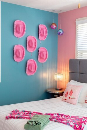 A bedroom with a bed, pillows, a nightstand, a lamp, and wall decorations including hats and disco balls.